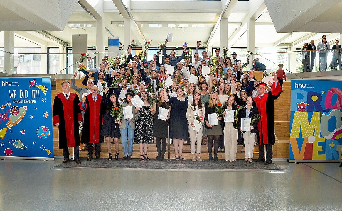 Gruppenbild aller Promovendinnen und Promovenden in festlicher Kleidung zusammen mit Dekan Prof. Klöcker und den Prodekanen Prof. Reifenberger und Prof. Mayatepek auf einer Treppe. 
