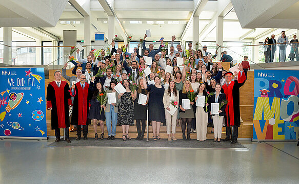 Gruppenbild aller Promovendinnen und Promovenden in festlicher Kleidung zusammen mit Dekan Prof. Klöcker und den Prodekanen Prof. Reifenberger und Prof. Mayatepek auf einer Treppe. 